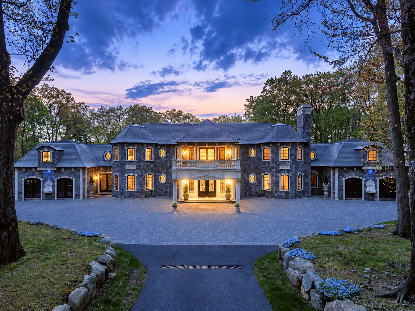 Illustrative image: a stone residence at dusk, with both wings framing an illuminated central entrance.