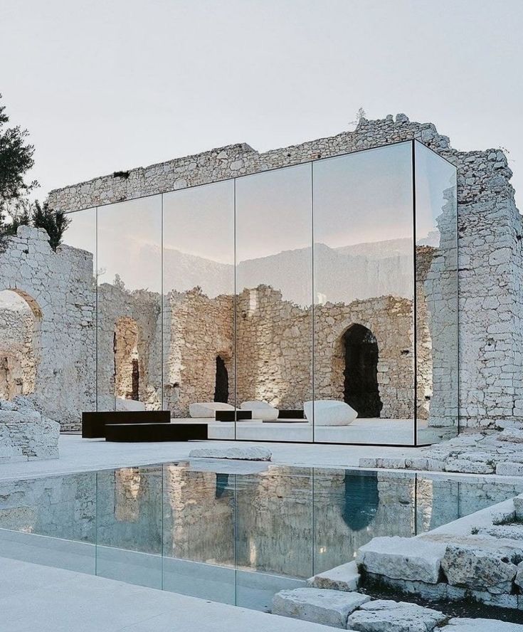 Reflective panels among pale masonry walls beside a reflecting pool.