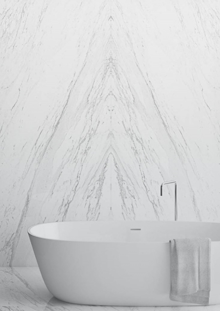 White stone walls with mirrored veining behind a freestanding bath