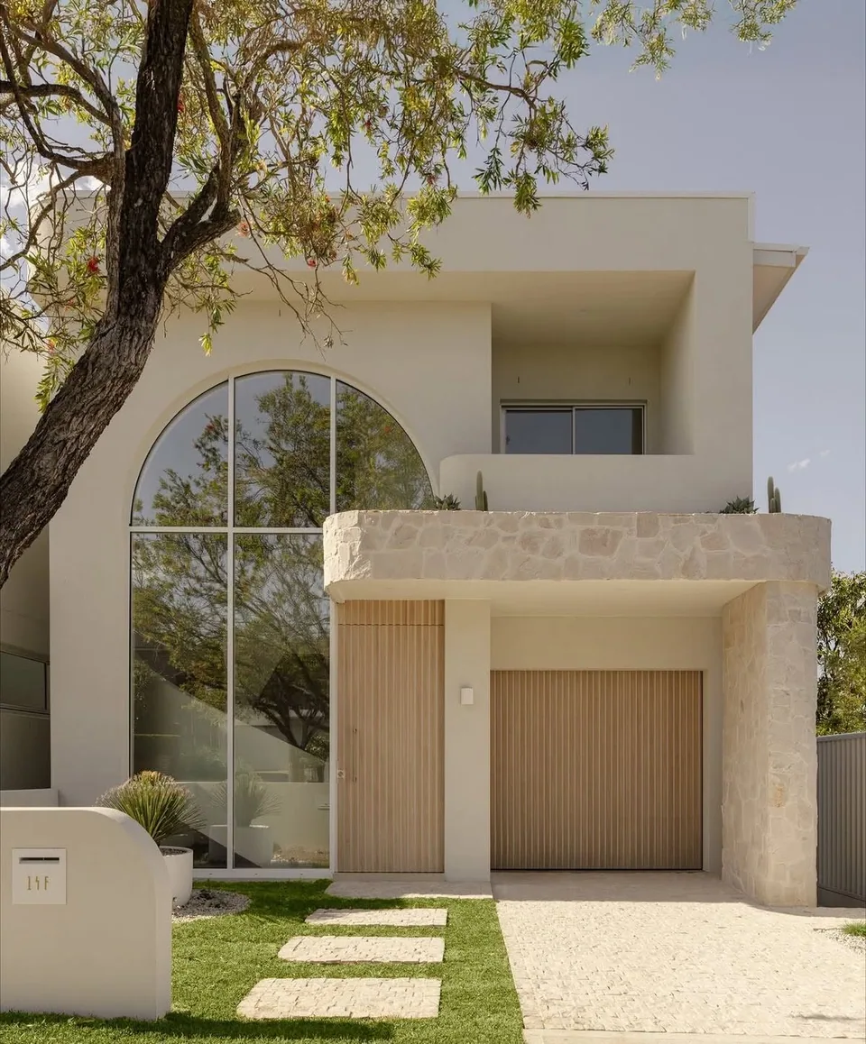 White two-story residence with an arched window, pale stone balcony, and tree in front
