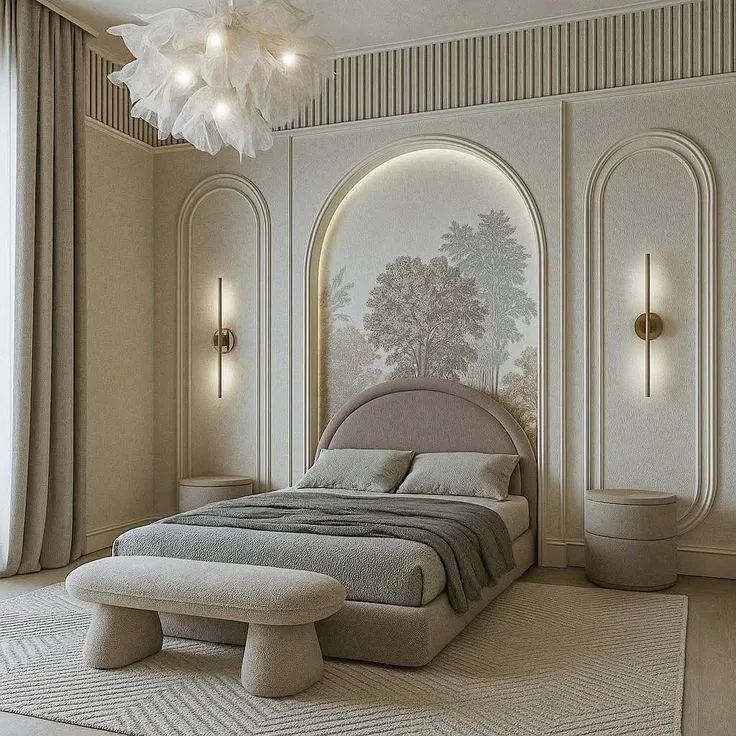 Neutral bedroom with an upholstered bed and bench, arched wall panels, tree-pattern mural, linear sconces, a gray rug, and a leaf-like ceiling light