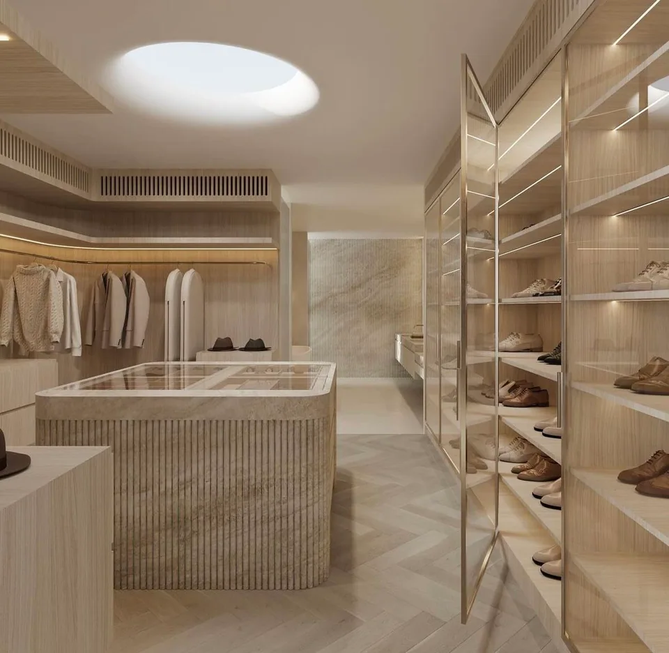 Skylit walk-in closet with a central glass-topped island, illuminated shelving, hanging rails, shoe storage, and pale herringbone flooring